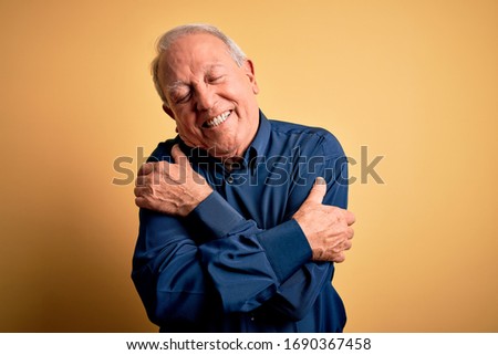 Grey haired senior man wearing casual blue shirt standing over yellow background Hugging oneself happy and positive, smiling confident. Self love and self care Сток-фото © 