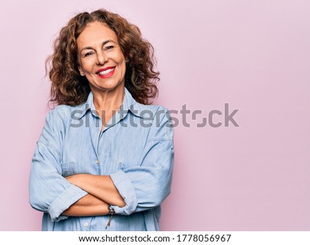 Middle age beautiful woman wearing casual denim shirt standing over pink background happy face smiling with crossed arms looking at the camera. Positive person.