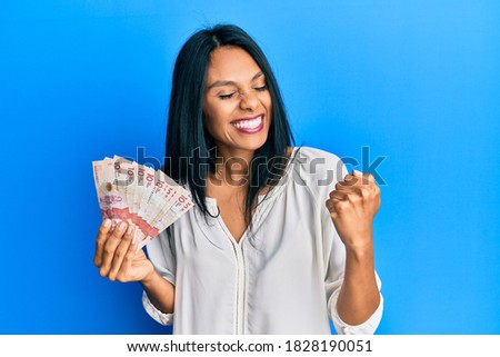 Young african american woman holding 10 colombian pesos banknotes very happy and excited doing winner gesture with arms raised, smiling and screaming for success. celebration concept.  Foto stock © 
