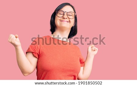 Brunette woman with down syndrome wearing casual clothes and glasses very happy and excited doing winner gesture with arms raised, smiling and screaming for success. celebration concept.  Stockfoto © 