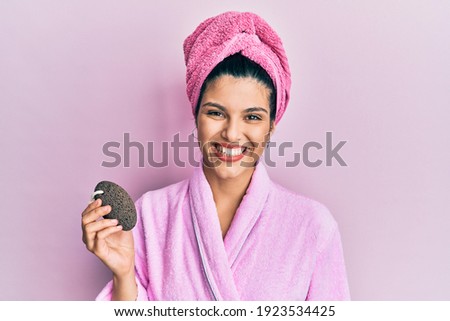 Young hispanic woman wearing shower bathrobe holding pumice stone looking positive and happy standing and smiling with a confident smile showing teeth  商業照片 © 