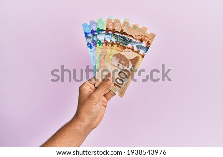 Hispanic hand holding canadian dollars banknotes over isolated pink background. Foto stock © 