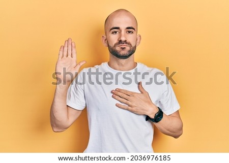 Young bald man wearing casual white t shirt swearing with hand on chest and open palm, making a loyalty promise oath  Foto stock © 