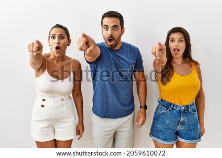 Group of young hispanic people standing over isolated background pointing with finger surprised ahead, open mouth amazed expression, something on the front  商業照片 © 