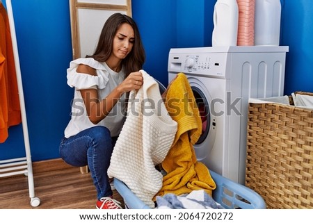 Young hispanic woman putting dirty laundry into washing machine skeptic and nervous, frowning upset because of problem. negative person.  Foto stock © 