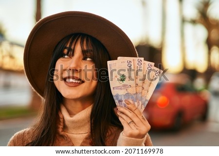 Brunette woman wearing winter hat smiling holding colombian pesos banknotes outdoors at the city on sunset Photo stock © 