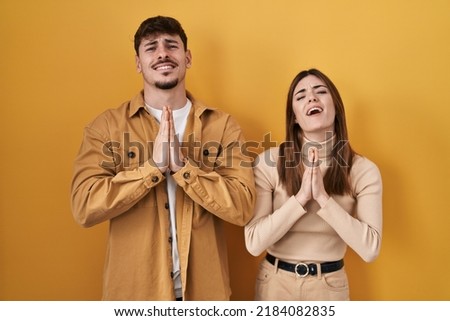 Young hispanic couple standing over yellow background begging and praying with hands together with hope expression on face very emotional and worried. begging.  Сток-фото © 