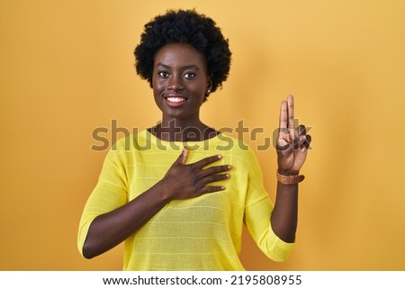African young woman standing over yellow studio smiling swearing with hand on chest and fingers up, making a loyalty promise oath  Foto stock © 