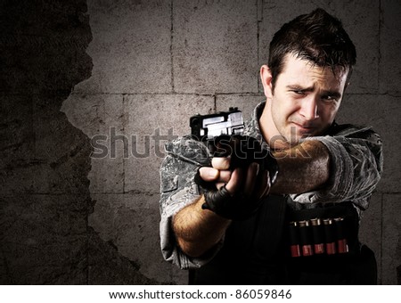 portrait of young soldier aiming with gun against a grunge bricks wall