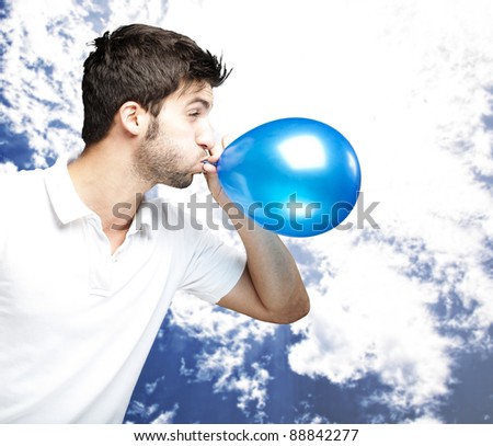 portrait of young man blowing a balloon against a cloudy sky background