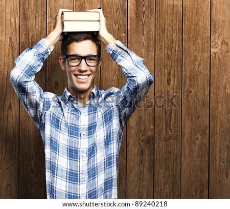 portrait of young man holding books on his head against a wooden wall