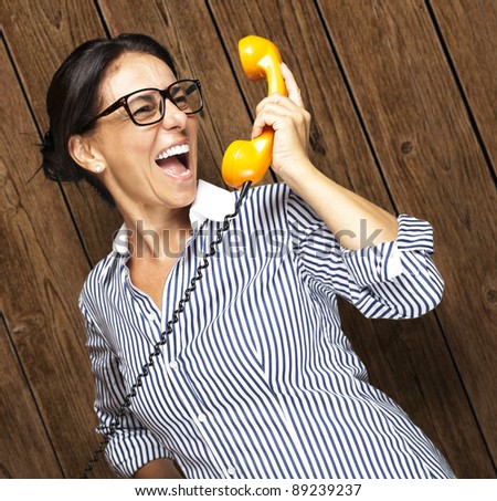 portrait of middle aged woman talking on vintage telephone against a wooden wall