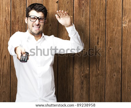 portrait of young man changing channel against a wooden wall