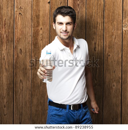 portrait of young man holding water bottle against a wooden wall