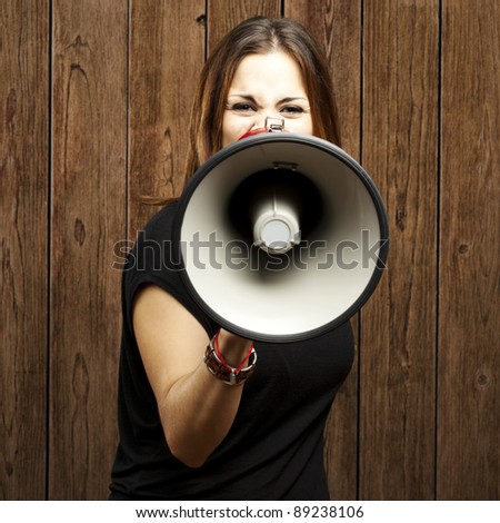 portrait of serious young woman shouting with megaphone against a wooden wall