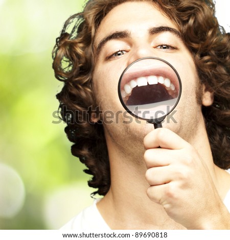 portrait of young man with magnifying glass showing his teeth against a nature background
