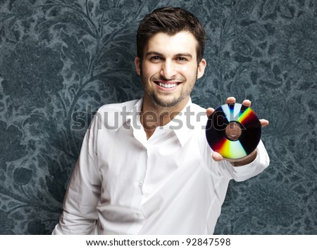 portrait of a handsome young man holding cd against a vintage wall