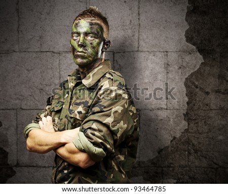 portrait of young soldier with jungle camouflage paint against a grunge bricks background