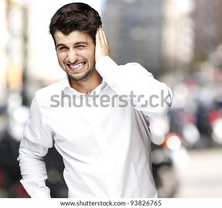 portrait of a young man irritated hearing a loud noise against a city background