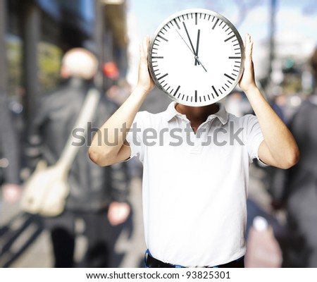 portrait of a man holding a big clock in front of his head at a crowded place