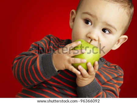 portrait of a handsome kid biting a green apple over red background