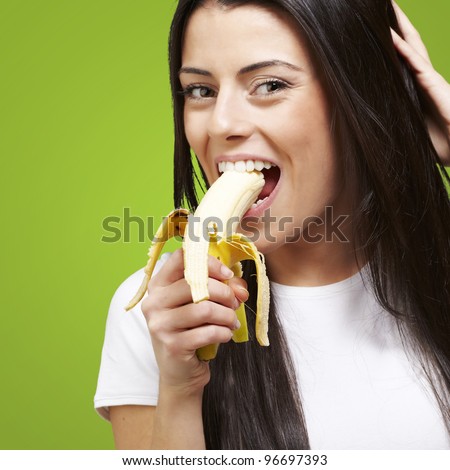 young woman eating a banana against a green background