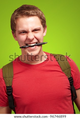 portrait of angry young man biting pen over green background