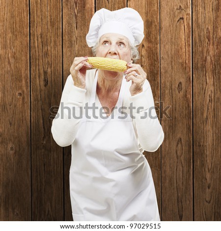 senior woman cook eating a corncob against a wooden background