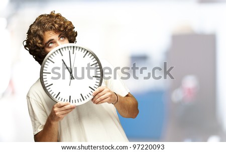 scared young man hidden behind a clock indoor