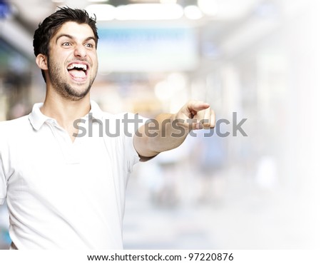 portrait of a handsome young man pointing and joking at a crowded place
