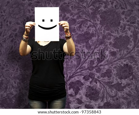 Woman showing a blank paper with a smile emoticon in front of her face against a vintage wall