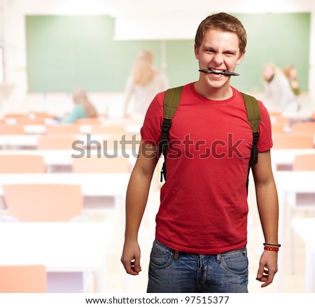 portrait of angry young man biting pen at classroom
