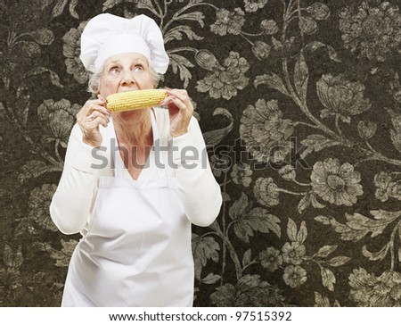 senior woman cook eating a corncob against a vintage background