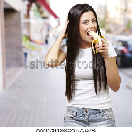 young woman eating a banana against a street background