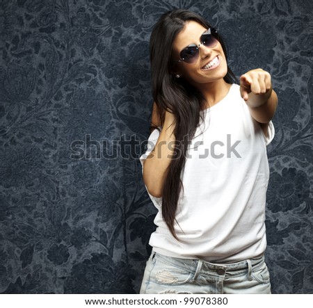 portrait of young woman wearing heart sunglasses pointing against a vintage wall