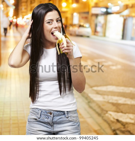 young woman eating a banana against a city night background