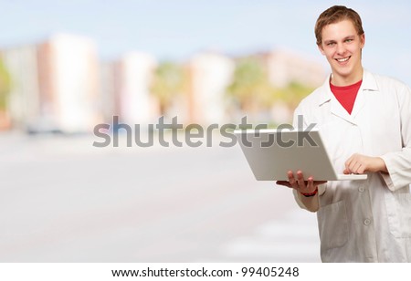 portrait of young student holding laptop against a cityscape