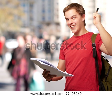 portrait of handsome student holding notebook and pen at crowded city