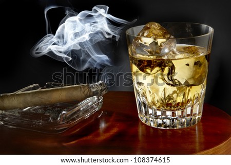 Glass of whiskey and lit cigar shot on wooden bar surface