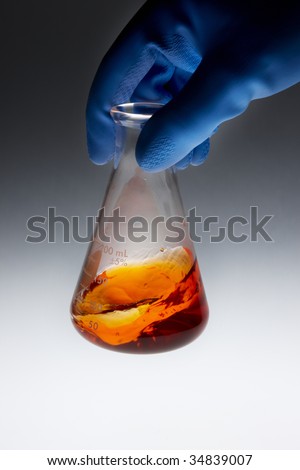 Gloved hand mixing beaker of orange chemicals