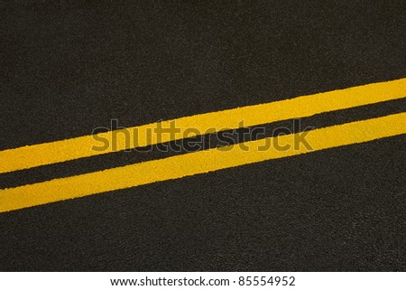 Close up of a black asphalt road with yellow stripes