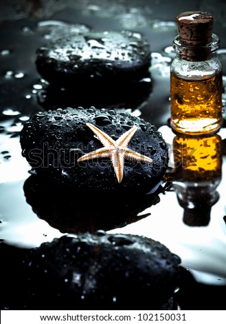 Starfish laying on a basalt stone and massage oils covered with water drops