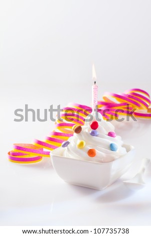 Party ice-cream dessert in a square dish with a single burning birthday candle and spirally coiled decorative ribbon with copy space