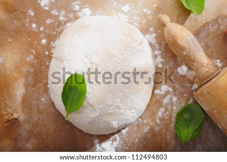 Fresh bread dough with a rolling pin on a wooden surface ready to be rolled out for a pizza base or pastry