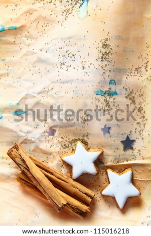 Grunge Christmas background with star-shaped cookies and stick cinnamon on aged stained crumpled paper strewn with small seeds with copyspace