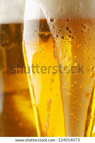 Closeup of a frothy cverflowing glass of golden ale or beer with liquid running down the outside of the glass, cropped view image
