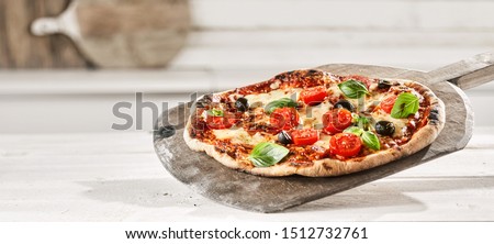 Tasty Margherita Italian Pizza with extra fresh tomato, olives and basil trimmings on an old wooden paddle straight from a wood fired oven, panorama banner format