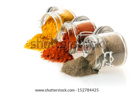 Colourful ground spices spilling from glass jars onto a white background with chilli pepper, curry powder and ground black pepper with copyspace