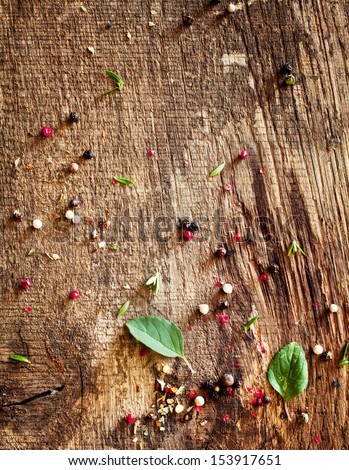 Scattered mixed peppercorns and basil lying on an old textured wooden surface in a country kitchen after preparing a meal