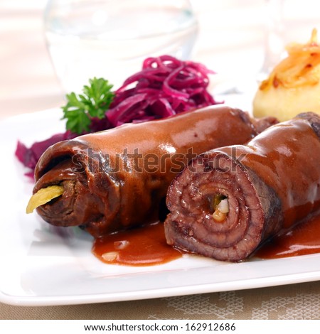 Two healthy lean beef roulades with thinly sliced meat rolled around a vegetable or pickle filling and served with cooked vegetables, close up view